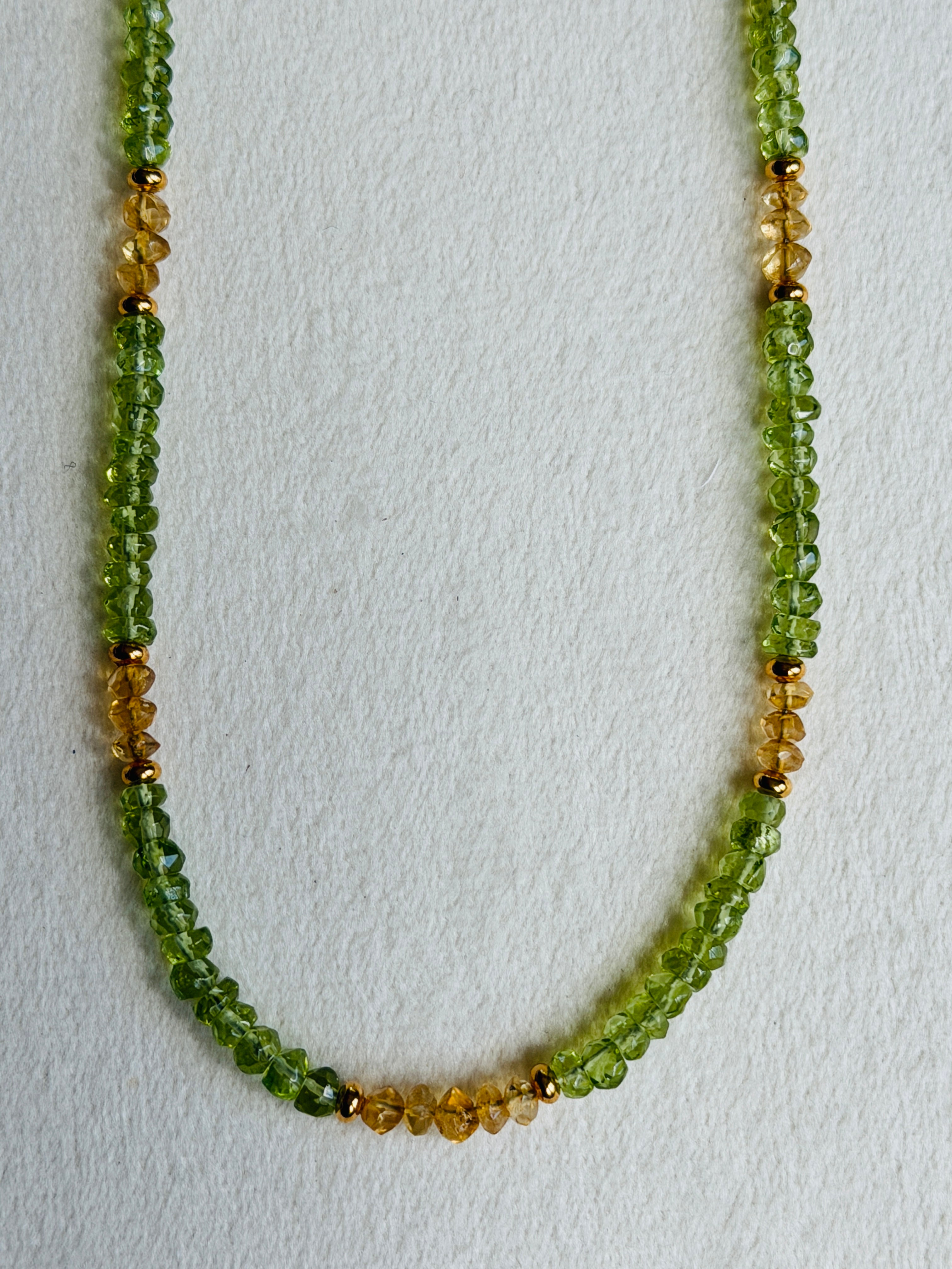 Necklace with green and gold beads on a light gray background
