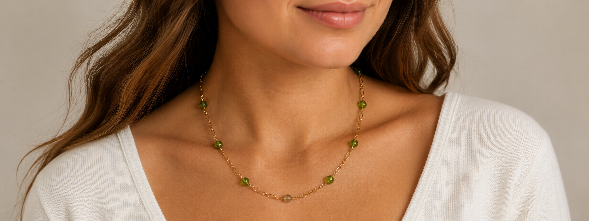 Close-up of a woman wearing a gold necklace with green beads against a neutral background