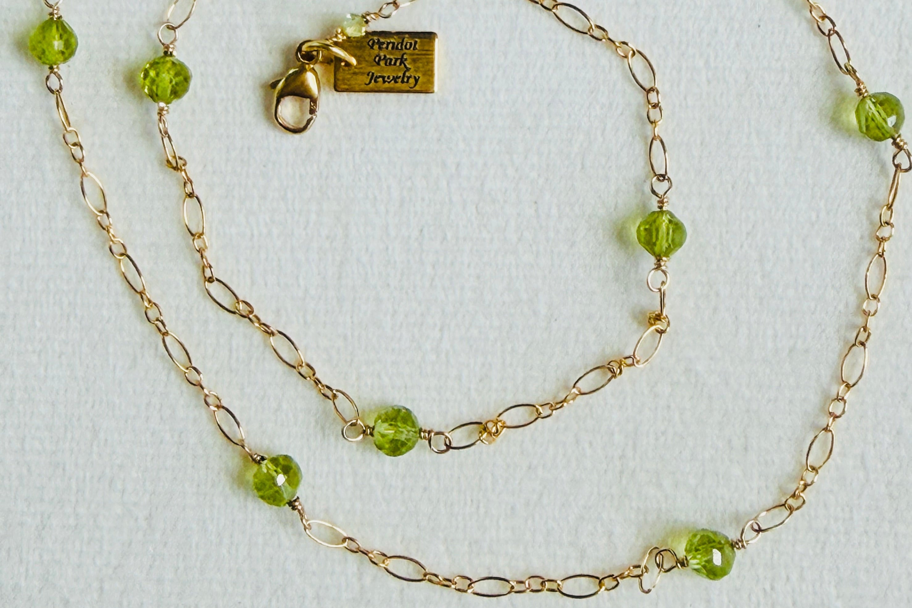 Gold chain necklace with green beads on a white background