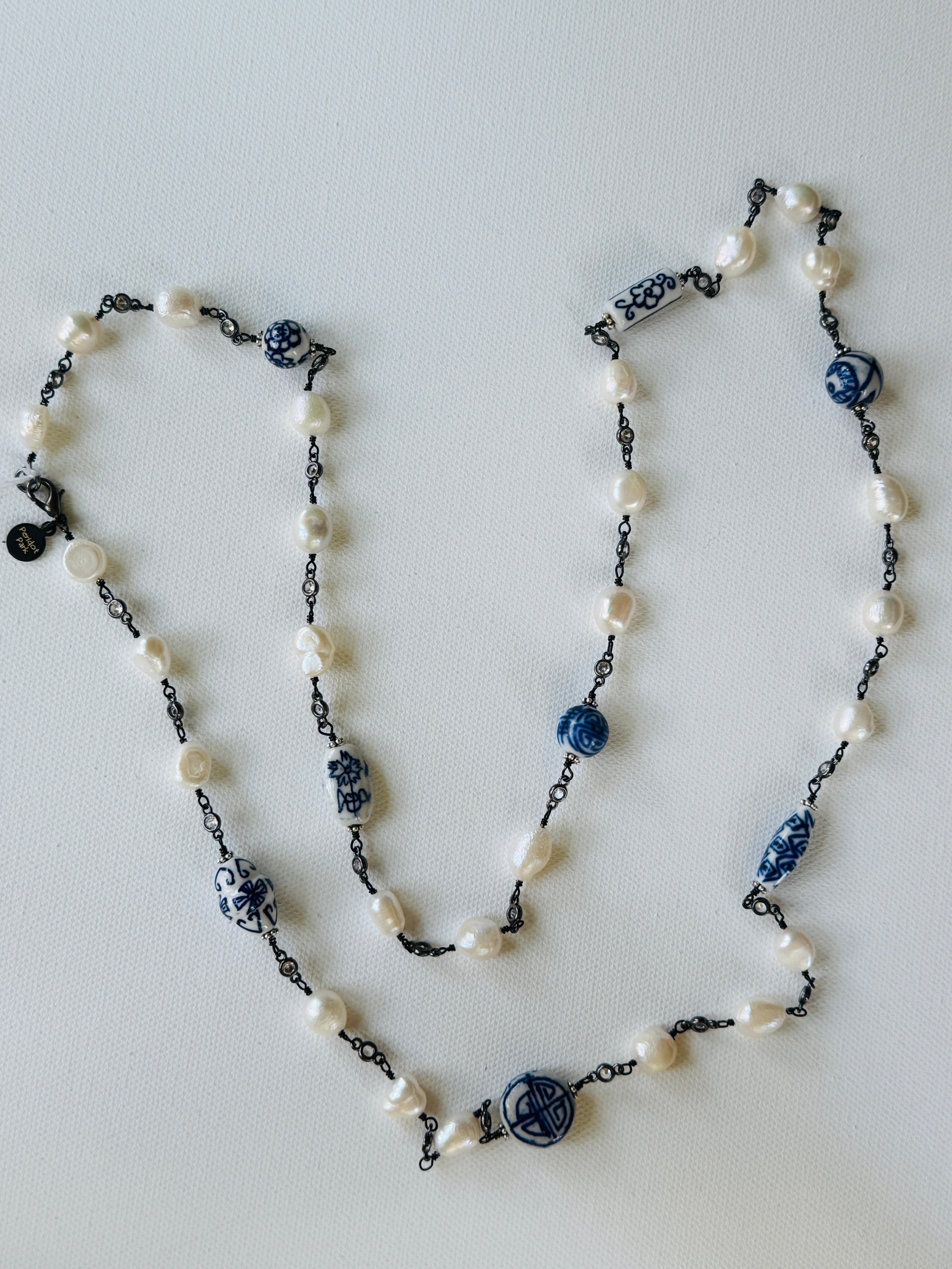 A beaded necklace with freshwater pearls, blue and white patterned ceramic beads, and dark metal chain links, displayed on a light gray background.